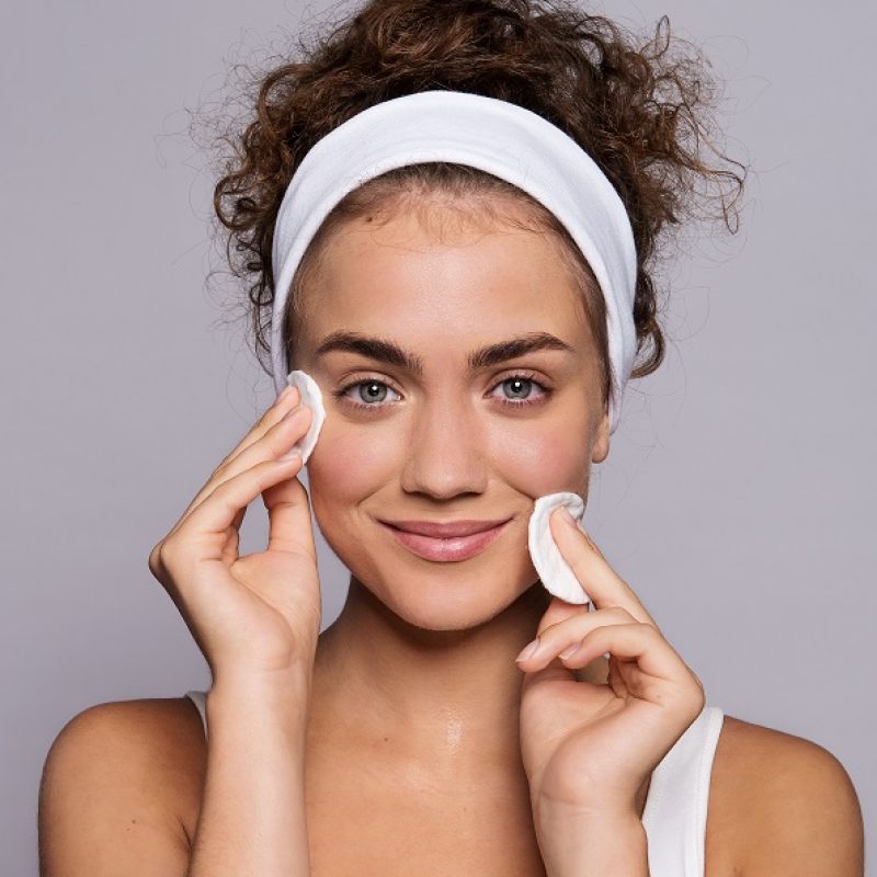 A portrait of a young woman cleaning face in a studio, beauty and skin care.
